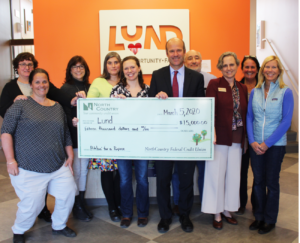Group of Lund staff with Bob Morgan with large check in front of Lund logo on orange background